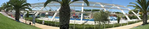 Vista panorâmica do parque aquático coberto com piscinas, palmeiras e estrutura de arcos brancos