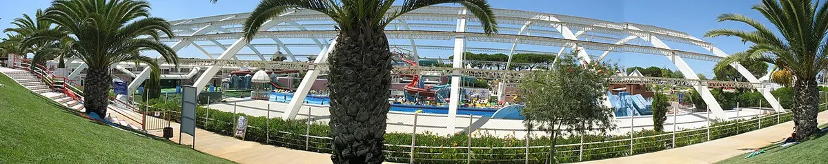 Vista panorâmica do parque aquático coberto com piscinas, palmeiras e estrutura de arcos brancos