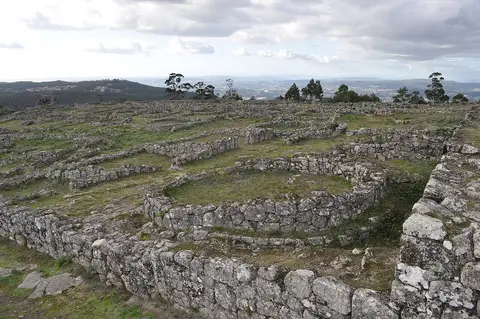 Ruínas circulares de pedra da Citânia de Sanfins, com vista sobre colinas ao fundo