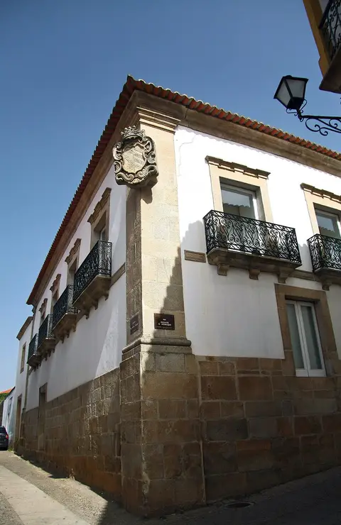 Edifício solarengo de esquina, com brasão em pedra e varandas de ferro forjado, em Torre de Moncorvo