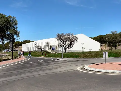 Edifício branco do Fluviário de Mora visto da estrada, rodeado de árvores e relva sob céu azul.
