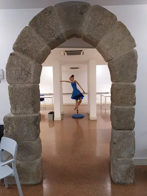 Interior da Biblioteca Lúcio Craveiro da Silva com arco de pedra e escultura de bailarina de vestido azul