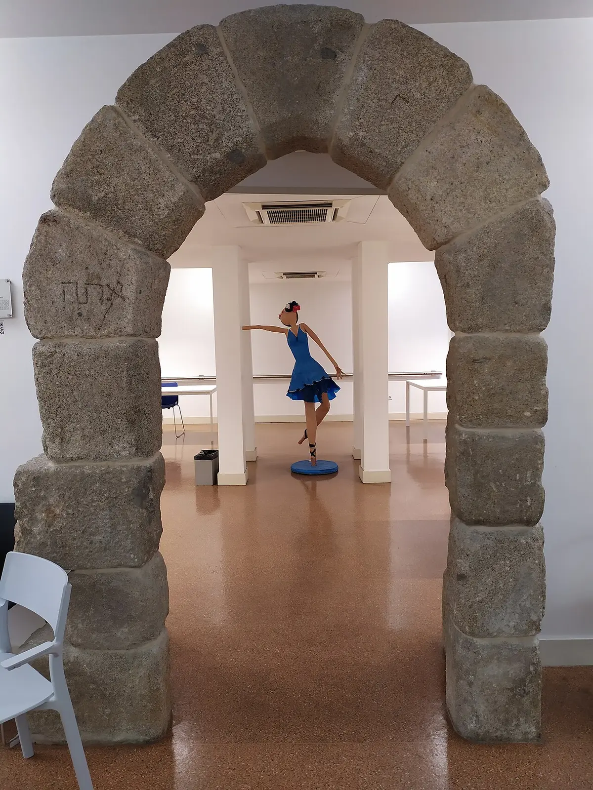 Interior da Biblioteca Lúcio Craveiro da Silva com arco de pedra e escultura de bailarina de vestido azul