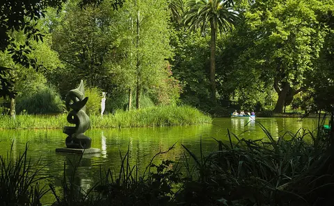 Lago do Parque Dom Carlos I com escultura moderna, vegetação densa e um barco ao fundo