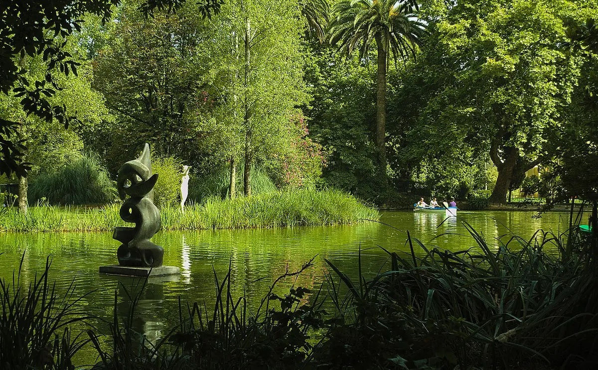 Lago do Parque Dom Carlos I com escultura moderna, vegetação densa e um barco ao fundo