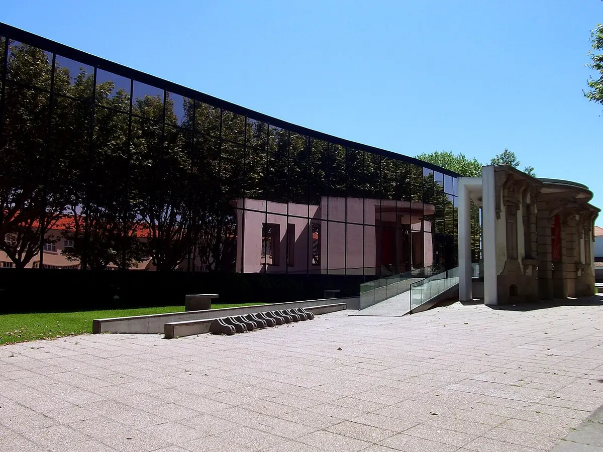Edifício moderno da Biblioteca Municipal Rocha Peixoto, com fachada de vidro escuro e pátio em pedra
