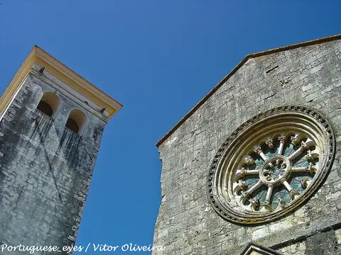 Fachada em pedra da Igreja de São João de Alporão, com rosácea gótica e torre sineira, vista de baixo.