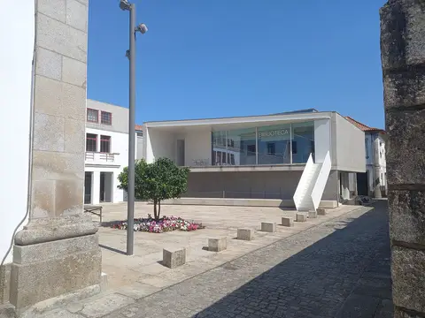 Edifício moderno da Biblioteca Municipal de Caminha, com letreiro em vidro e largo empedrado em frente.