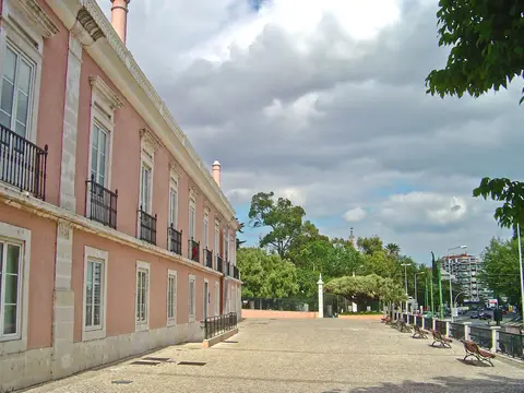 Fachada rosada do Palácio Ribamar em Algés, com esplanada calcetada e bancos ao lado.