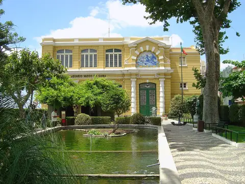 Fachada amarela do Aquário Vasco da Gama com tanque de água e jardim em frente