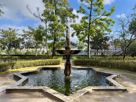 Fonte com estátua num tanque em forma de estrela, rodeada de buxo e árvores, no jardim do palácio