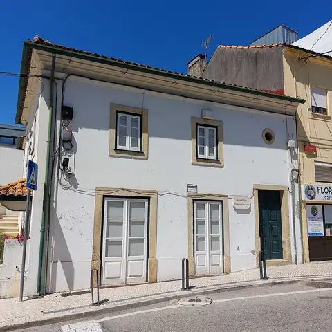 Fachada branca da Casa Museu Fernando Namora, com porta verde e janelas, sob céu azul.