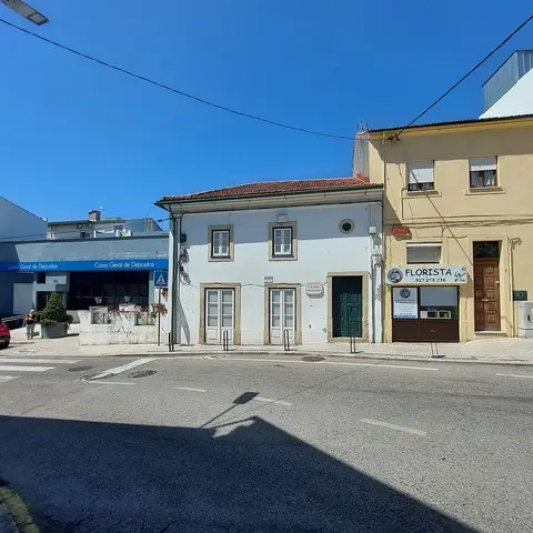 Fachada branca da Casa Museu Fernando Namora, junto a edifícios com florista, à beira da estrada