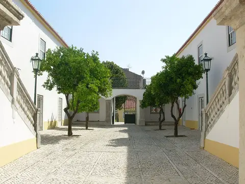 Pátio empedrado com laranjeiras e portão em arco, na Casa da Cerca, em Almada