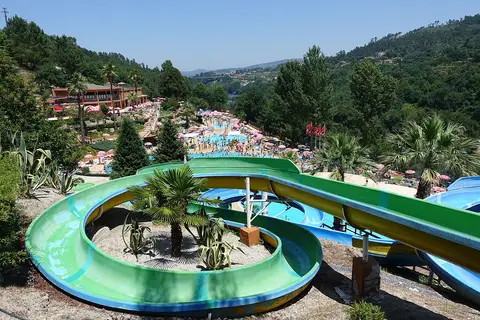 Vista panorâmica do parque aquático com escorregas coloridos, piscinas e vegetação em redor