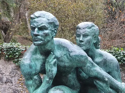 Escultura em bronze de duas figuras humanas, obra de Pedro Anjos Teixeira, ao ar livre entre vegetação