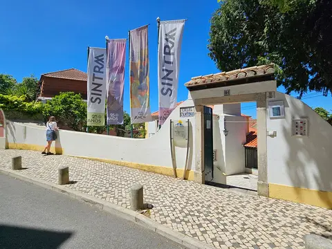 Entrada do Museu Ferreira de Castro em Sintra, com bandeiras e portão branco junto à calçada