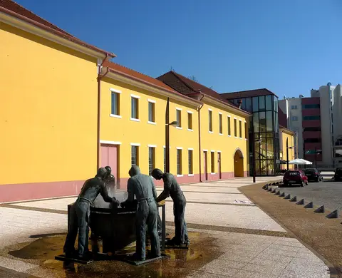 Edifício amarelo do Museu da Chapelaria com escultura em bronze de operários numa praça