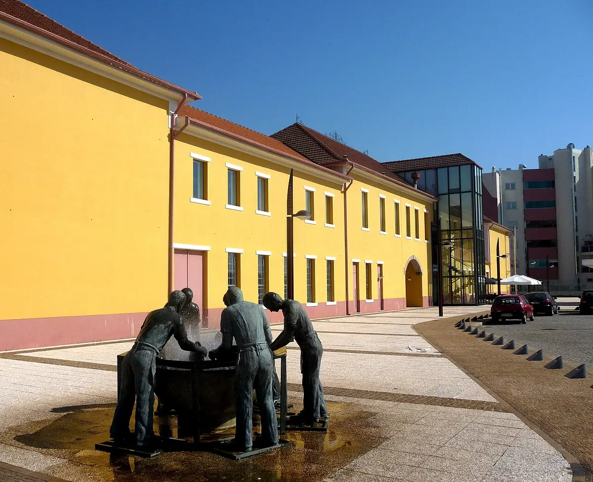 Edifício amarelo do Museu da Chapelaria com escultura em bronze de operários numa praça