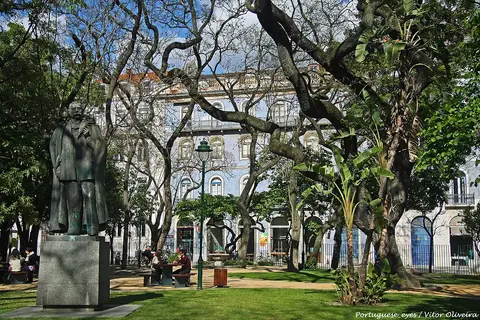 Jardim de Santos, em Lisboa, com estátua, relvado, árvores e edifícios em redor