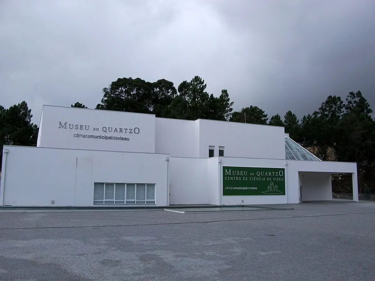 Fachada branca do Museu do Quartzo, em Viseu, com letreiro e árvores ao fundo