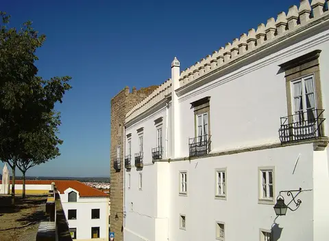 Fachada branca do Palácio dos Duques de Cadaval, em Évora, com varandas de ferro e torre medieval.