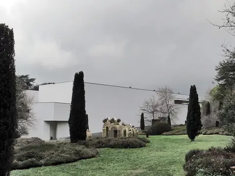 Edifício branco do Museu de Serralves visto do jardim, com ciprestes e relva em dia nublado