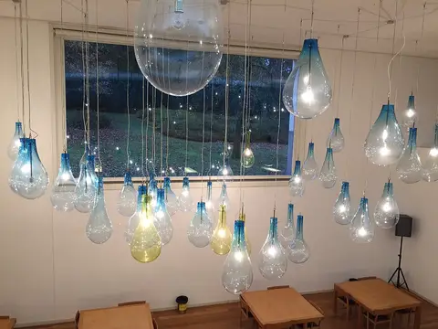 Instalação de candeeiros de vidro em forma de gota suspensos numa sala com mesas de madeira