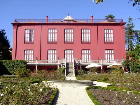 Fachada posterior cor-de-rosa da Casa Andresen, com jardim, canteiros e fonte circular em frente.
