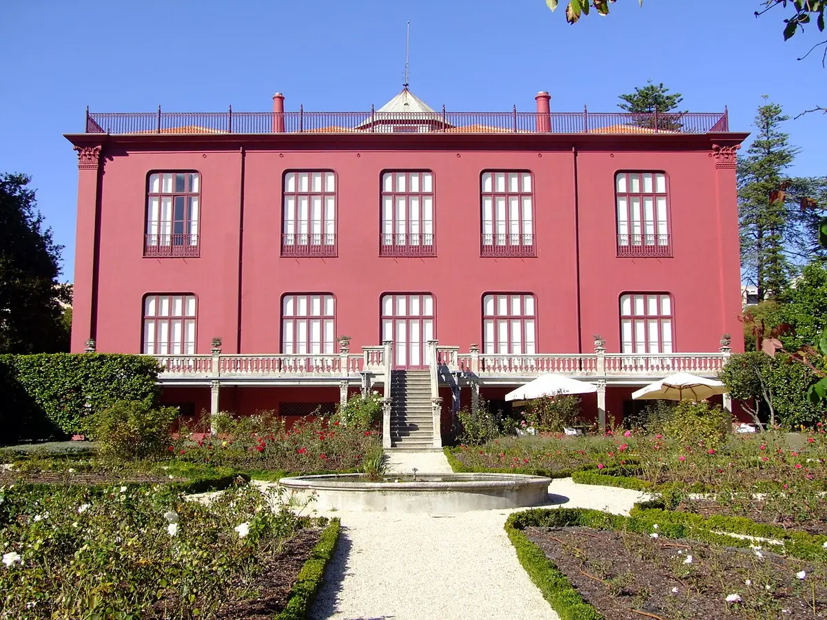 Fachada posterior cor-de-rosa da Casa Andresen, com jardim, canteiros e fonte circular em frente.