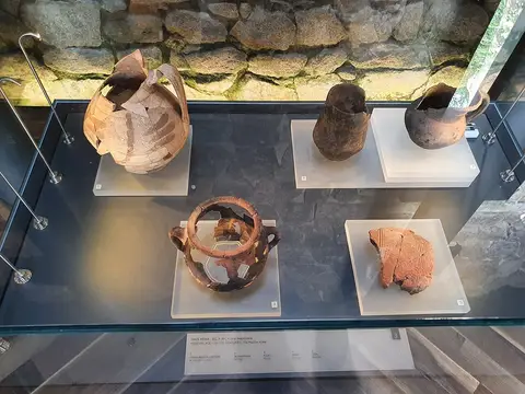 Vitrina museológica com peças de cerâmica medieval islâmica sobre suportes brancos, junto a muro de pedra.