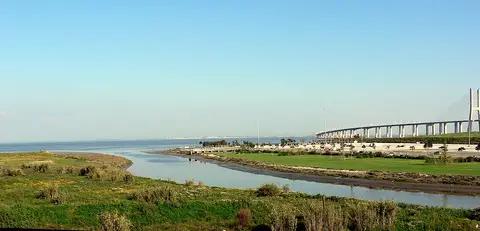 Foz do rio Trancão junto ao Parque Tejo, com relvados e a Ponte Vasco da Gama ao fundo