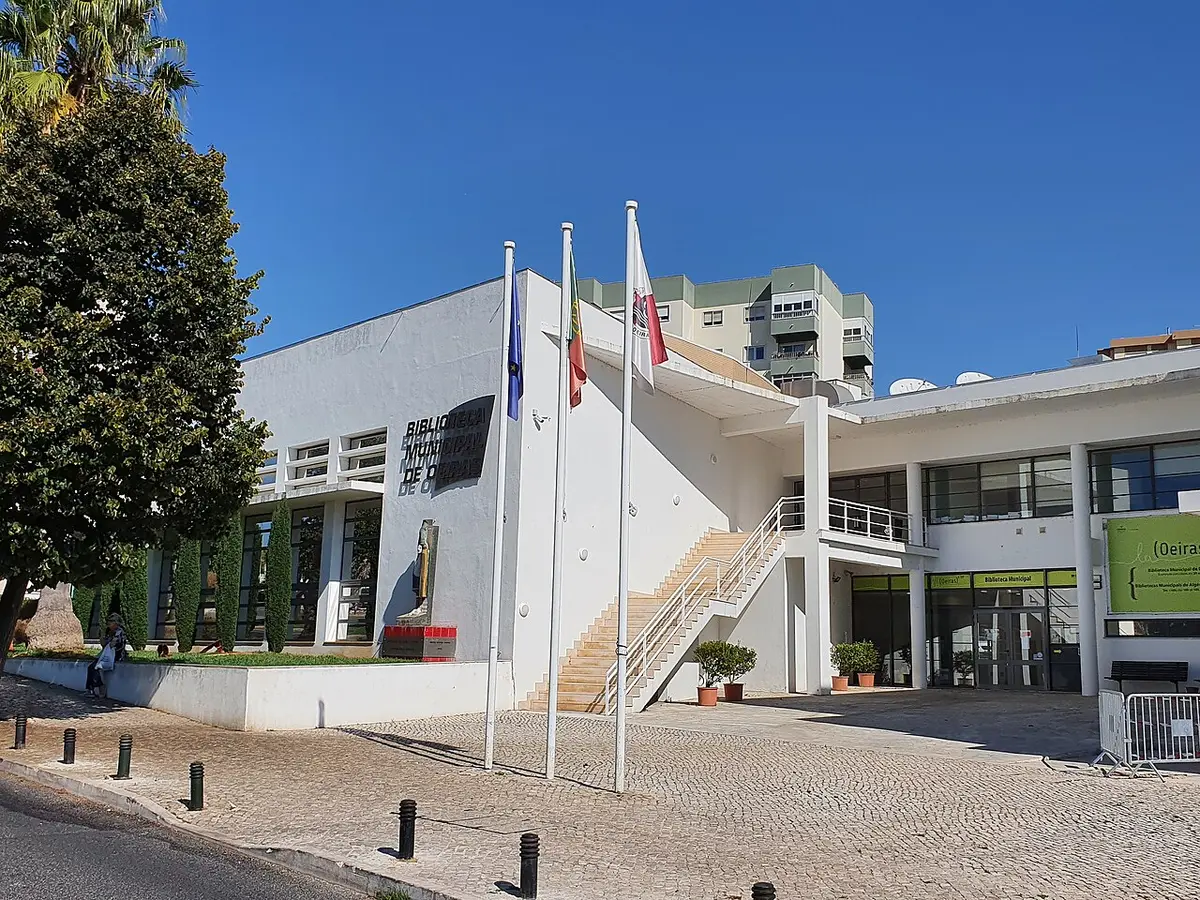 Edifício branco moderno da Biblioteca Municipal de Oeiras com bandeiras e escadaria exterior