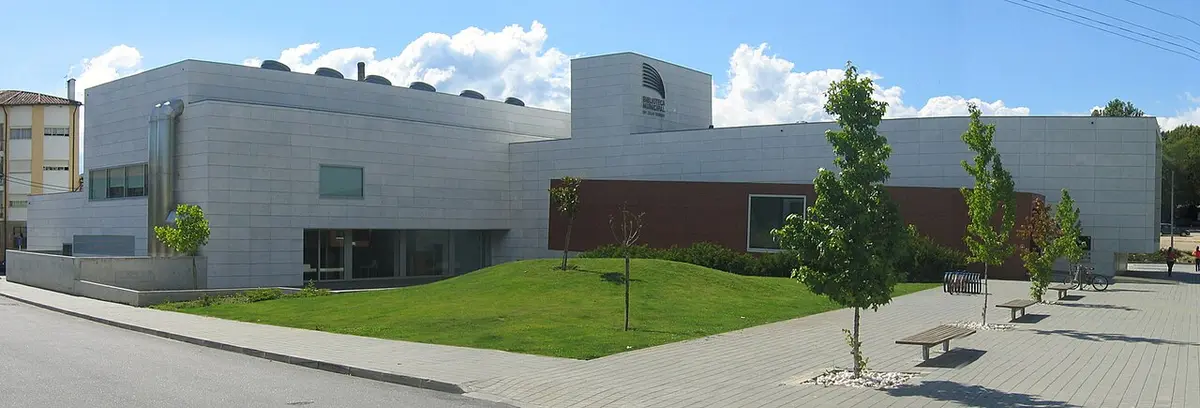 Exterior moderno da Biblioteca Municipal, com fachada clara, relvado e árvores jovens