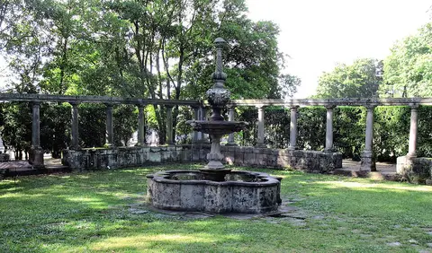 Fonte de pedra rodeada de relva e colunata em jardim arborizado da Quinta da Conceição