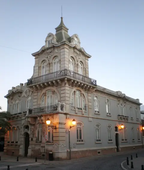 Fachada do Palacete Belmarço em Faro, edifício de estilo arte nova com varandas de ferro forjado, ao anoitecer