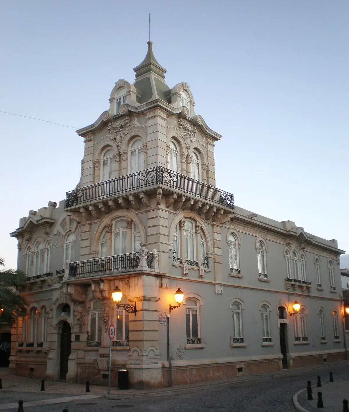 Fachada do Palacete Belmarço em Faro, edifício de estilo arte nova com varandas de ferro forjado, ao anoitecer