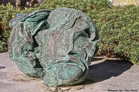 Escultura em bronze com pátina esverdeada, homenagem ao ator José de Castro, junto a arbustos num jardim