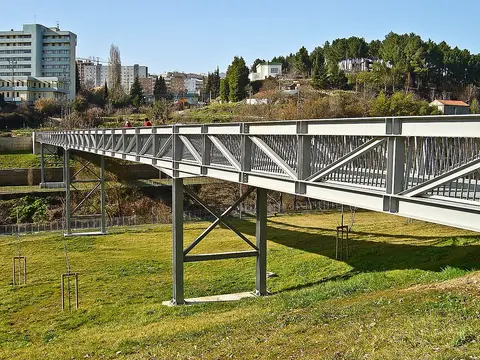 Passadiço metálico sobre relvado no Parque Urbano do Corgo, em Vila Real, com a cidade ao fundo