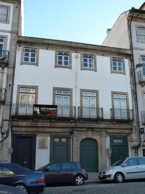 Fachada de edifício histórico de três pisos com varandas de ferro e portas verdes, no Porto.