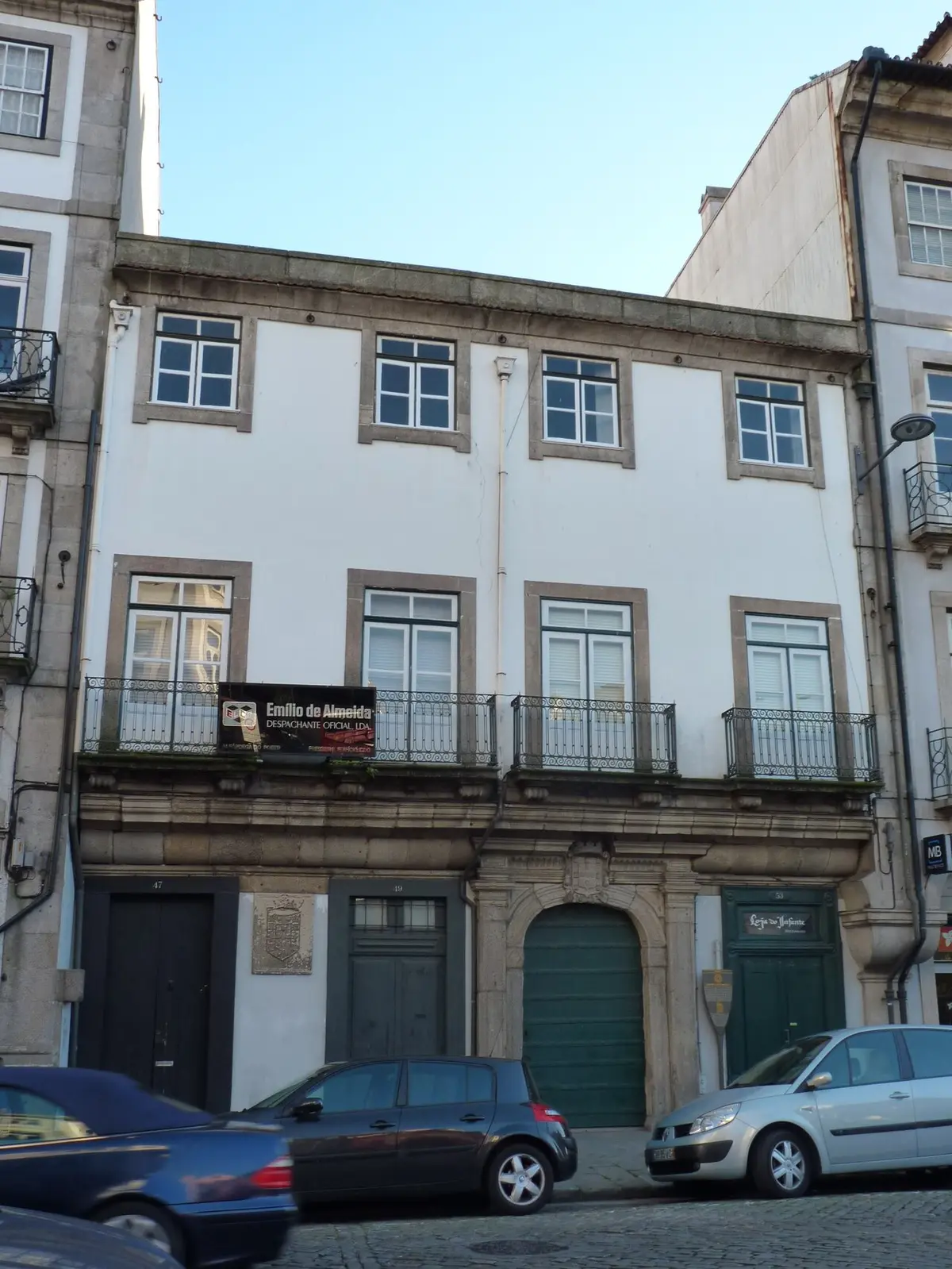 Fachada de edifício histórico de três pisos com varandas de ferro e portas verdes, no Porto.