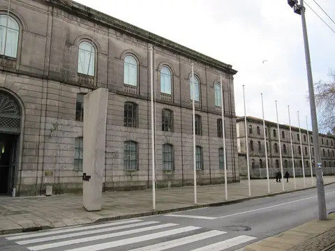 Fachada em pedra do Museu dos Transportes e Comunicações, no Porto, com mastros e passadeira em primeiro plano