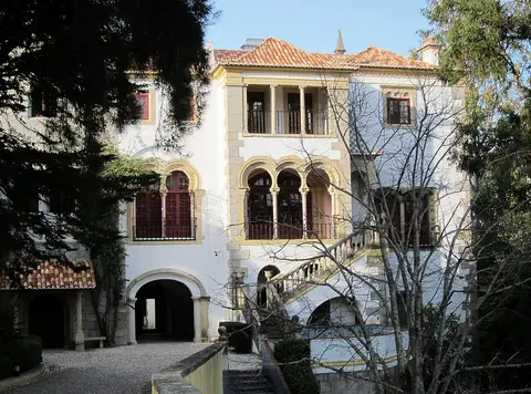 Fachada branca da Casa Verdades Faria, com janelas em arco e escadaria, rodeada de árvores