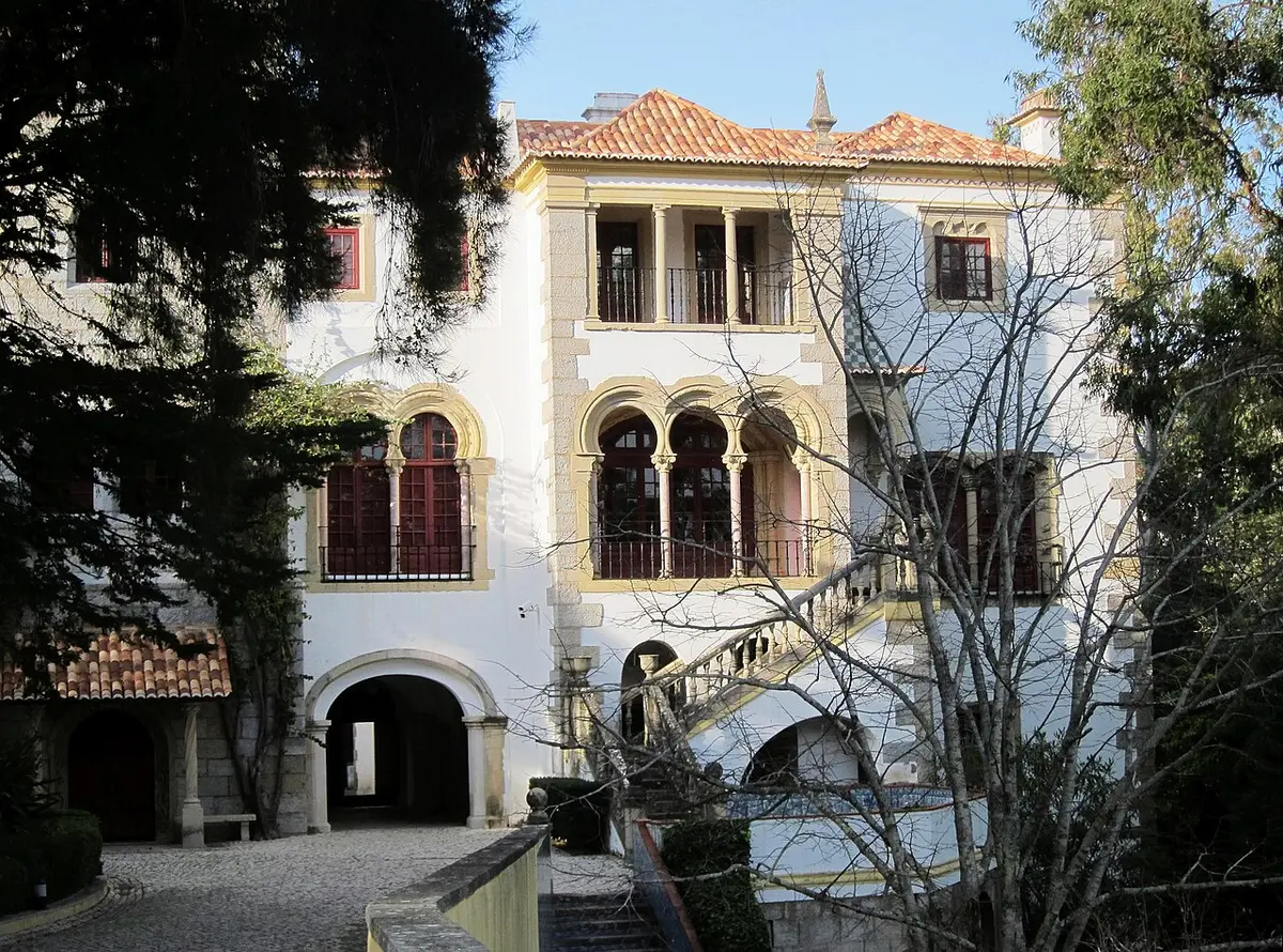 Fachada branca da Casa Verdades Faria, com janelas em arco e escadaria, rodeada de árvores
