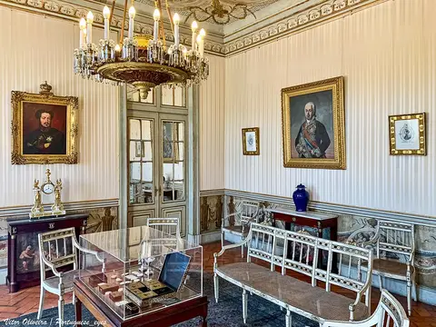 Sala do Palácio Nacional de Queluz com lustre, retratos a óleo e mobiliário de época.