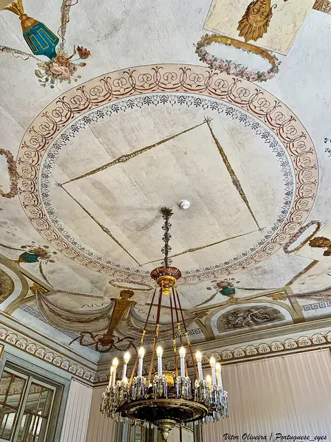 Teto pintado com decoração neoclássica e lustre de velas numa sala do Palácio Nacional de Queluz