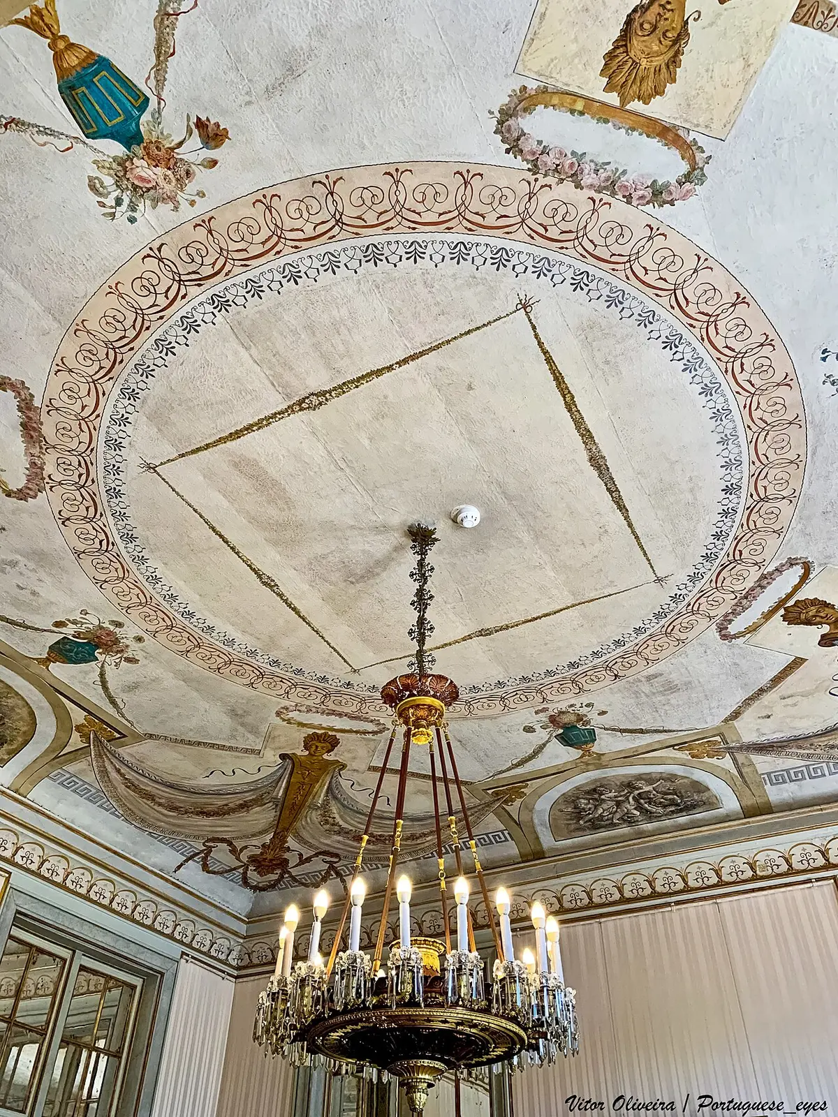 Teto pintado com decoração neoclássica e lustre de velas numa sala do Palácio Nacional de Queluz
