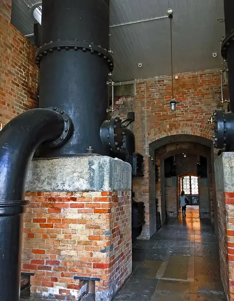 Interior industrial do Museu da Água, com grandes tubagens metálicas e paredes de tijolo