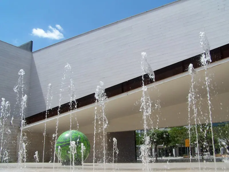 Fachada do Pavilhão do Conhecimento com repuxos de água e esfera verde em primeiro plano