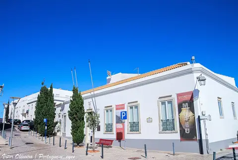 Edifício branco do Museu Municipal de Arqueologia de Albufeira, com cartazes na fachada e céu azul